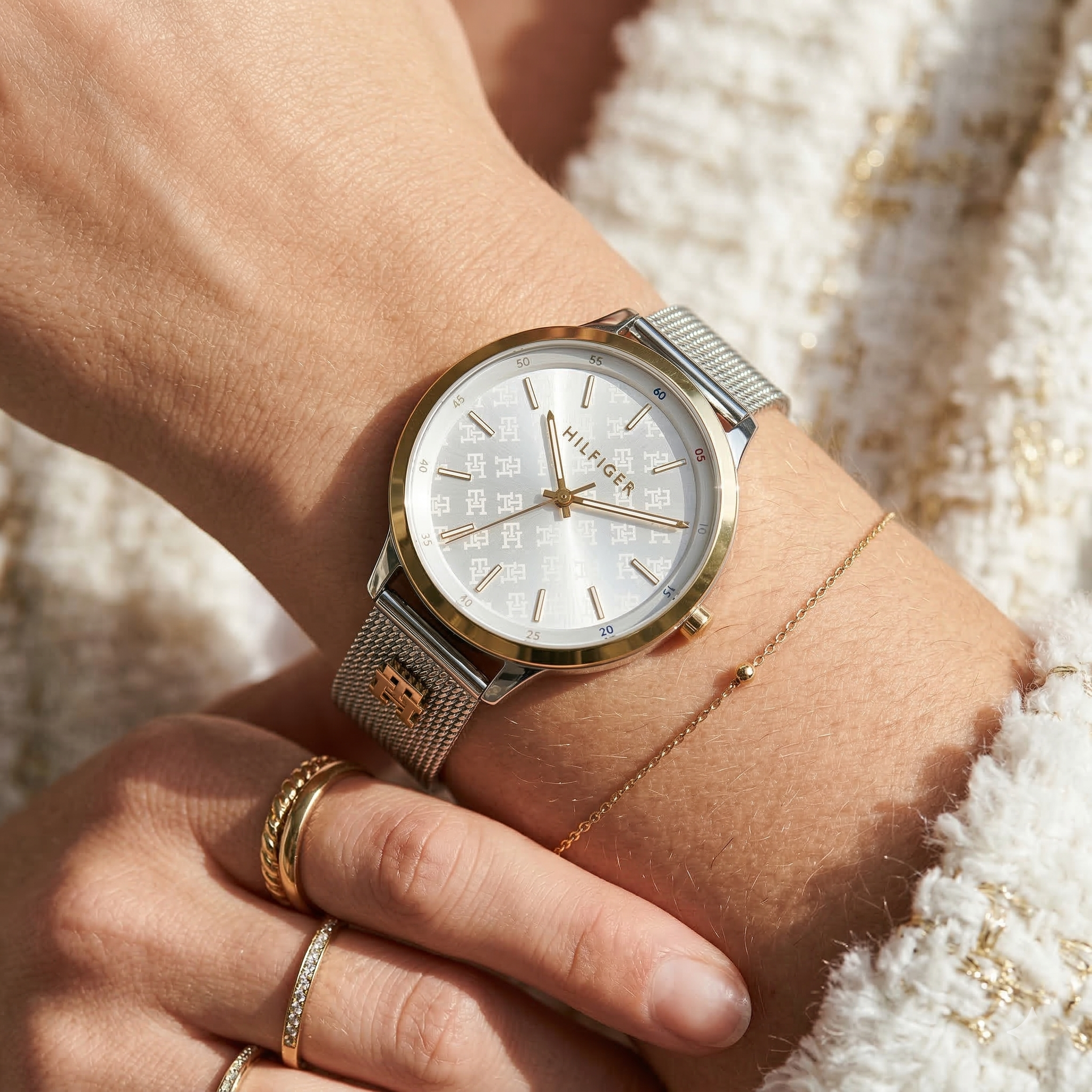 Close up of Tommy Hilfiger 1782586 women's quartz battery watch on wrist showing white monogram dial and silver mesh bracelet