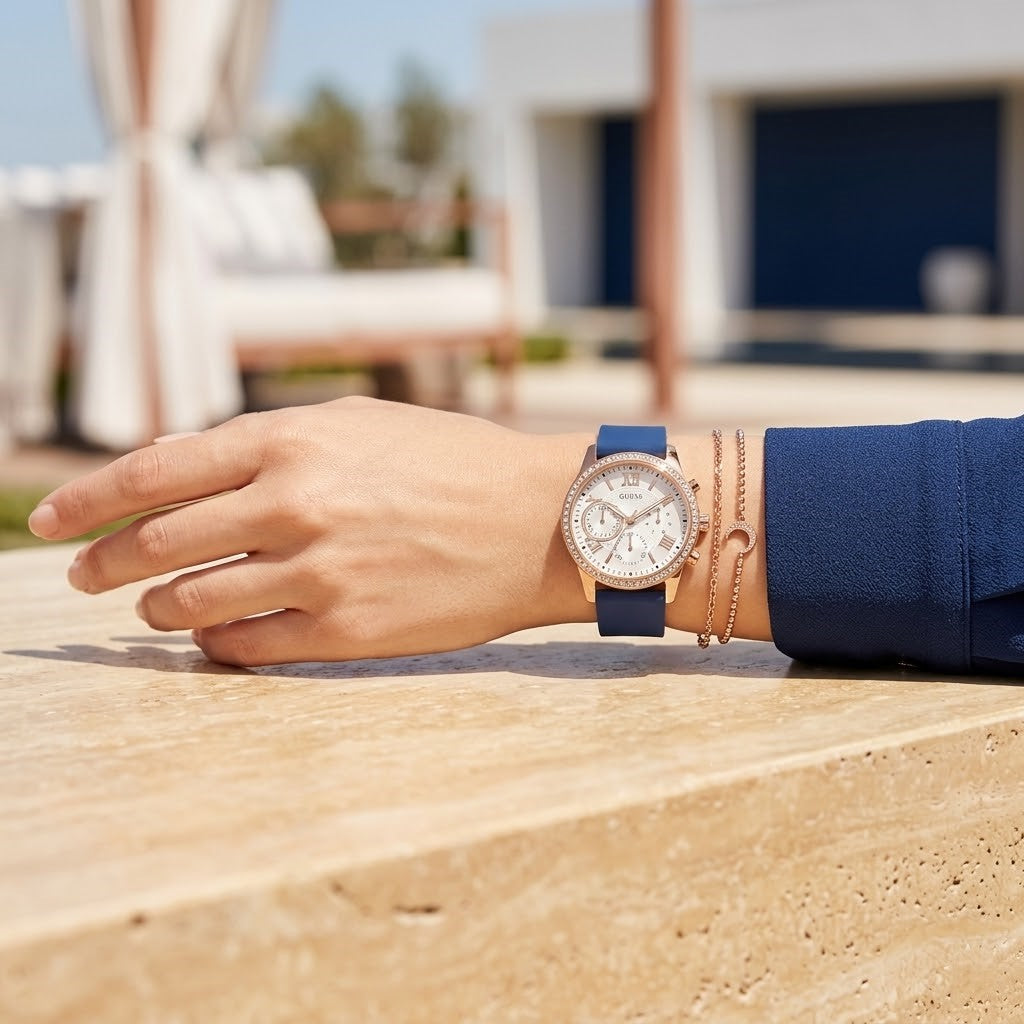 Close up of Guess Solar W1135L3 women's quartz battery multi-function watch (Gold Case and Royal Blue Rubber Strap variant) on wrist showing deep silver-white dial with multi-function display and luminous indices