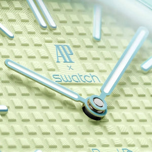 Close-up of a watch face with 'AP x Swatch' branding on a textured green background