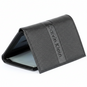 Perspective view of a standing semi-open Calvin Klein men's black saffiano leather flap wallet, displaying the front debossed logo and a glimpse of the clear ID window inside
