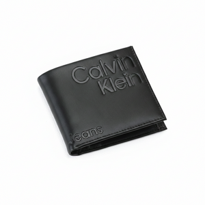 High-angle view of a closed Calvin Klein Jeans men's black genuine leather wallet showcasing the large debossed Calvin Klein logo and Jeans lettering on the front cover