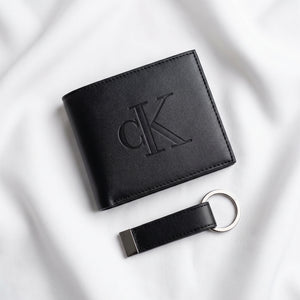 Studio product view of the Calvin Klein mirror original smooth black leather bifold wallet with large debossed center CK logo next to its matching standalone premium leather keychain