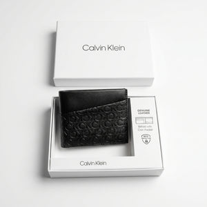Top-down studio product photography of the Calvin Klein smooth black leather bifold wallet neatly resting inside its custom white branded packaging