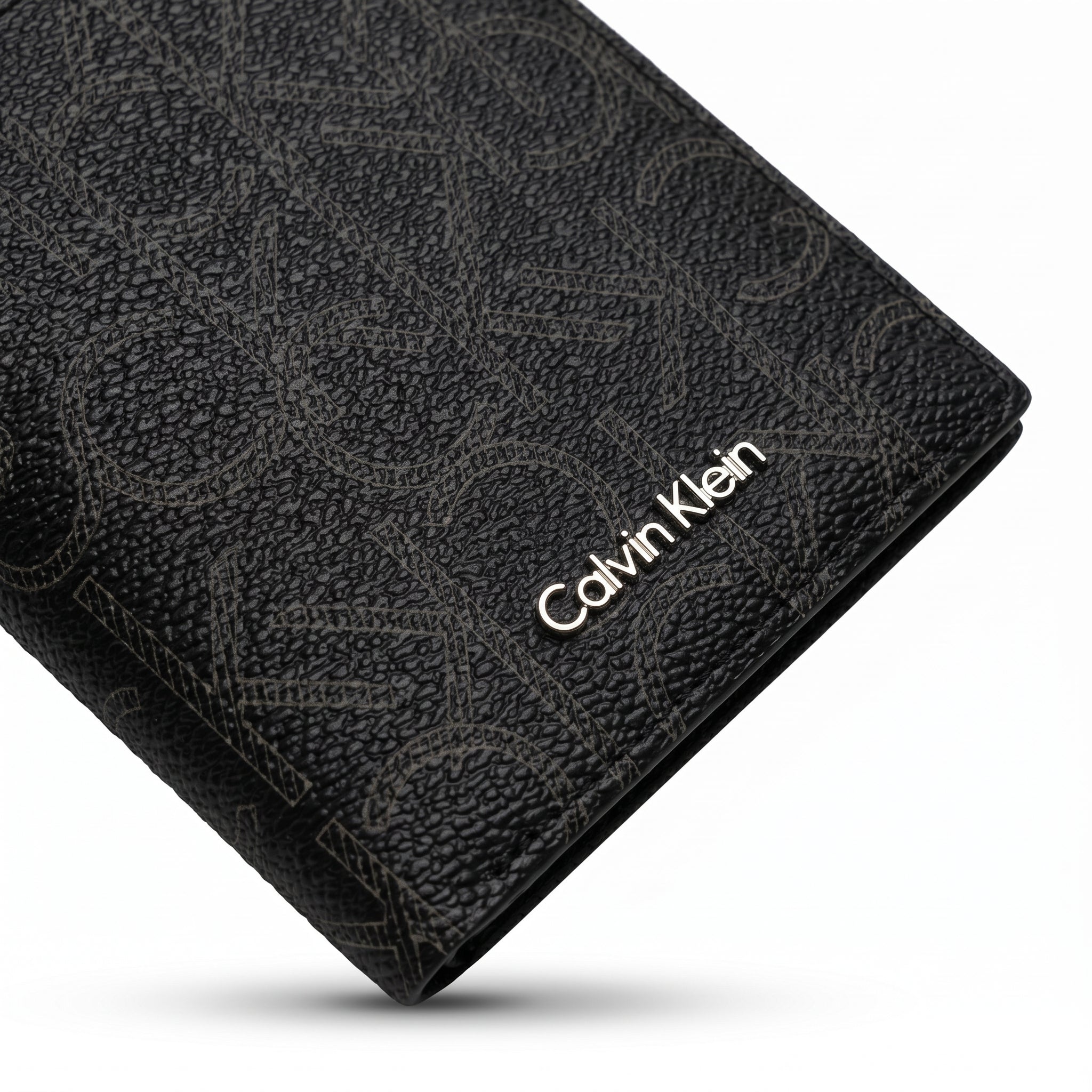 Macro close-up studio shot focusing on the round silver metal CK hardware logo and vertical stitching details over black smooth genuine leather