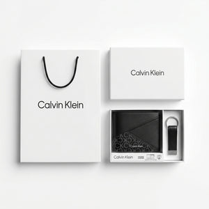 Top-down studio product photography of the Calvin Klein mirror original smooth black leather wallet and matching keychain set neatly arranged inside its open white branded gift box