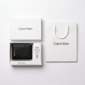 Full premium packaging presentation of the Calvin Klein mirror original pebbled black leather trifold wallet alongside its white gift box and matching shopping bag