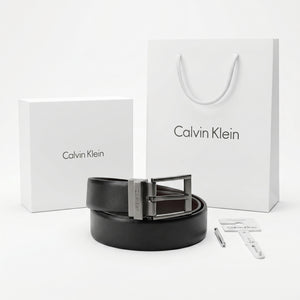 Full premium packaging presentation of the Calvin Klein mirror original reversible smooth black leather belt alongside its white gift box, matching shopping bag, tags, and hole punch tool