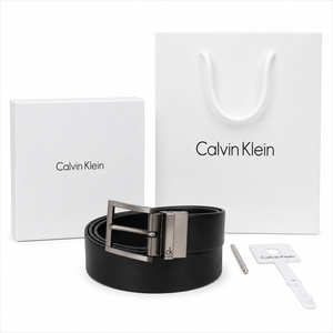 Full premium packaging presentation of the Calvin Klein mirror original reversible leather belt with its white gift box, matching shopping bag, tags, and hole punch tool