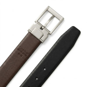 Live close-up smartphone photograph of the Calvin Klein mirror original reversible belt highlighting the disassembled gunmetal buckle with vertical logo alongside the brown leather side with embossed brand stamp