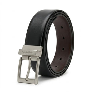 Studio product photograph of the Calvin Klein mirror original reversible leather belt coiled in an oval shape showcasing the smooth black leather and rotatable gunmetal buckle with vertical logo