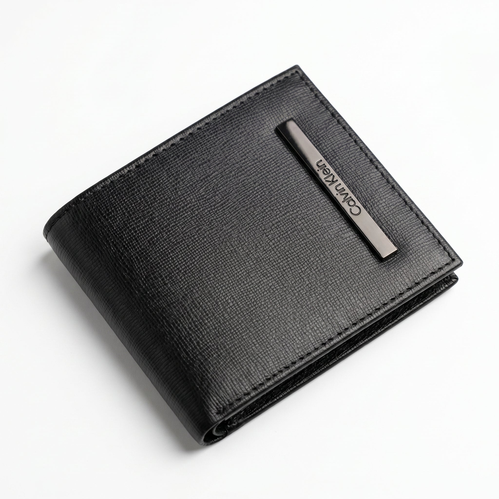 Macro close-up studio shot focusing on the engraved vertical silver metal Calvin Klein logo plate over the scratch-resistant black textured leather surface