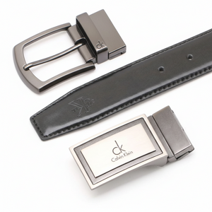 High-detail close-up of two Calvin Klein metal buckles showing the embossed brand logo on the black leather strap and the polished gunmetal hardware finish