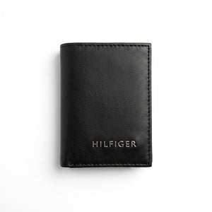 Straight front view product photography of the Tommy Hilfiger black leather trifold wallet showcasing smooth finish and silver metal Hilfiger lettering
