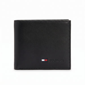 Straight front view product photography of the Tommy Hilfiger black smooth leather wallet highlighting the vertical woven signature stripe and metal flag logo