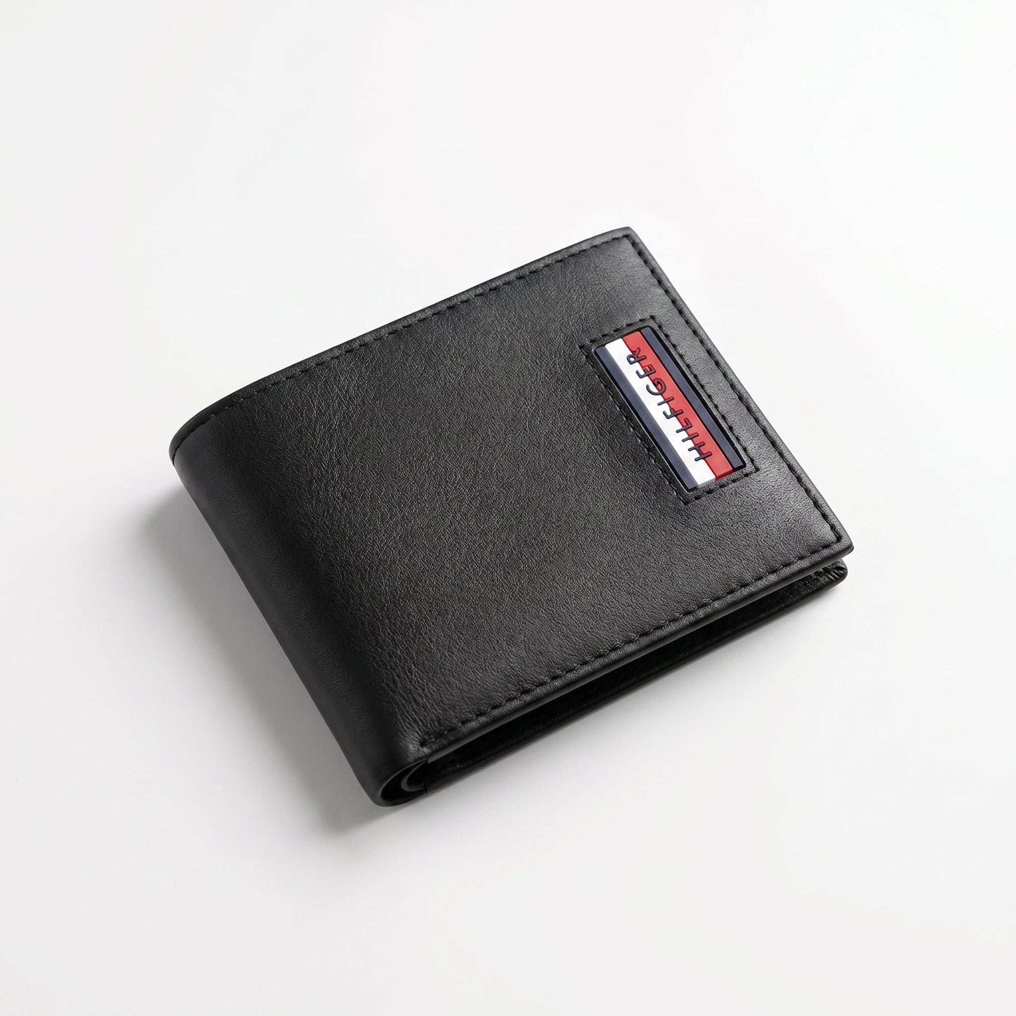 Macro close-up shot focusing on the embedded Tommy Hilfiger metal flag logo, fine stitching, and the contrast between saffiano and smooth leather textures