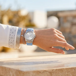 Half-face lifestyle shot of a woman with fair skin wearing bracelets and rings on the same hand as the Guess Limelight sky blue rubber watch for a sophisticated everyday look