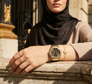 Elegant woman wearing Guess Venus GW0118L1 women's quartz battery watch with gold case and luxury black rubber strap