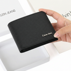 Hand holding a closed Calvin Klein men's black saffiano leather wallet featuring a silver metal logo, displayed above its original open white branded gift box