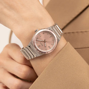 A close-up of a wrist wearing a BOSS watch with a silver-toned metal link bracelet and a dusty pink dial and bezel.