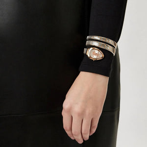 Hand wearing a black sleeve with gold bracelets on a plain background