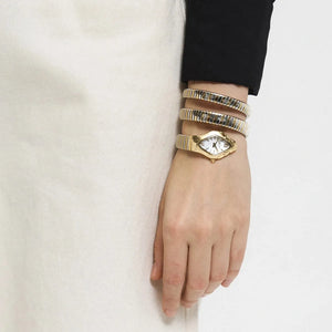 Hand wearing a gold watch and bracelets on a plain background