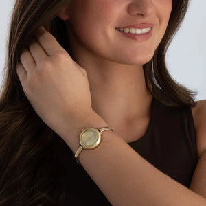 Woman wearing a gold watch on her wrist with a plain background