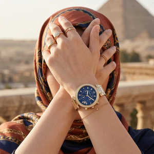 Elegant woman wearing Michael Kors Parker MK6262 women's quartz battery watch with gold-tone case and luxury navy blue dial