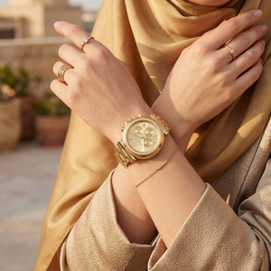Elegant woman wearing Michael Kors Maren MK7493 women's quartz battery watch with gold-tone case and luxury logo bezel