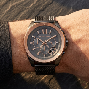 Close up of Michael Kors Brecken MK8868 men's quartz battery watch on wrist showing grey sunray dial and rose gold bezel contrast