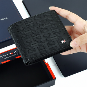 Handheld view of a Tommy Hilfiger men's Black leather wallet, showing its compact size and the premium silver metal flag emblem
