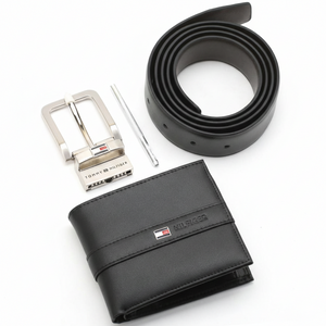 Side perspective of a standing Tommy Hilfiger black leather bifold wallet next to a rolled leather belt and a polished silver metal buckle