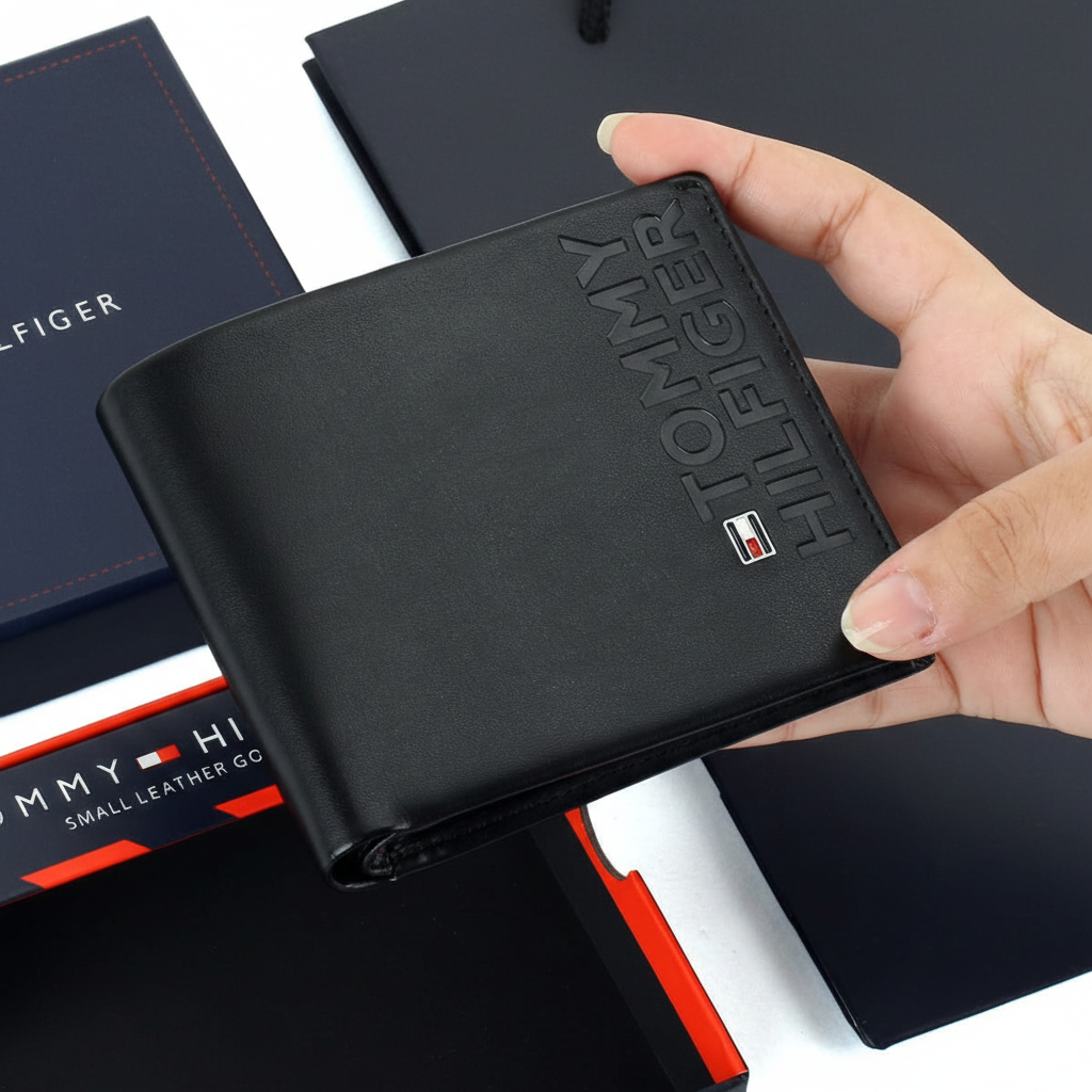 Hand holding a Tommy Hilfiger black smooth leather wallet featuring a large embossed vertical logo and the iconic small enamel flag