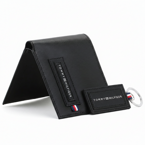 Perspective view of a standing Tommy Hilfiger men's black leather wallet featuring a stitched front logo patch, displayed next to a matching leather keychain