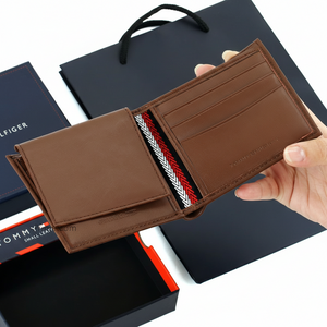 Handheld display of an open Tommy Hilfiger brown leather wallet, showcasing the internal compartments and embossed brand name