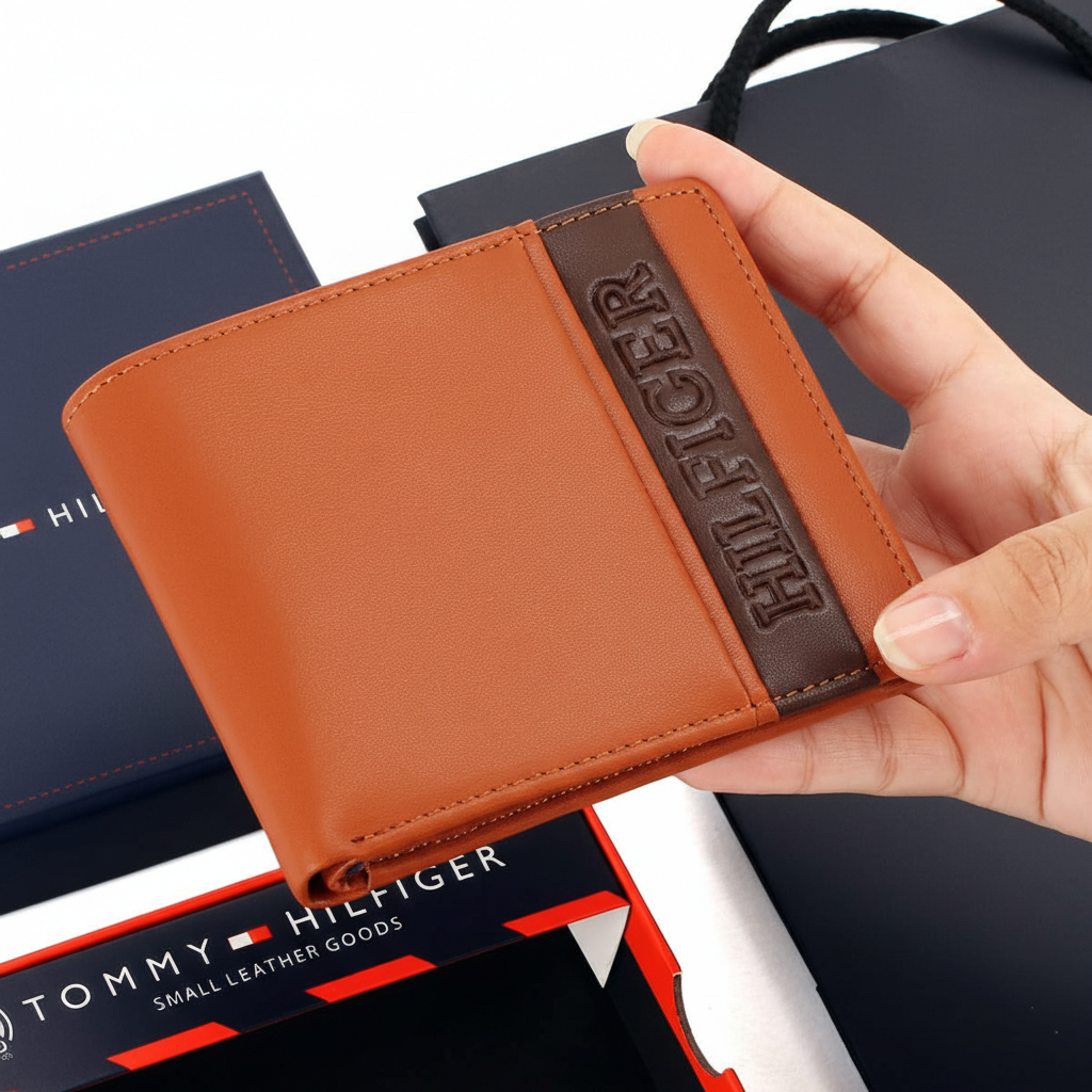 Handheld view of a Tommy Hilfiger camel genuine leather bifold wallet highlighting the high-quality smooth texture and vertical HILFIGER branding
