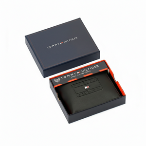 Authentic Tommy Hilfiger men's black genuine leather bifold wallet featuring an embossed flag box logo, displayed in its premium navy branded gift box