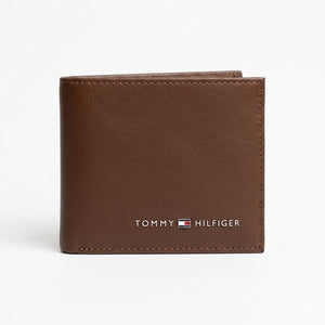 Straight front view product photograph of the Tommy Hilfiger mirror original smooth brown leather bifold wallet showcasing the enamel flag and silver branding