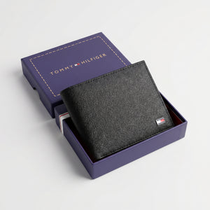Top-down studio product photography of the Tommy Hilfiger mirror original textured black leather wallet neatly resting inside its open premium navy branded gift box
