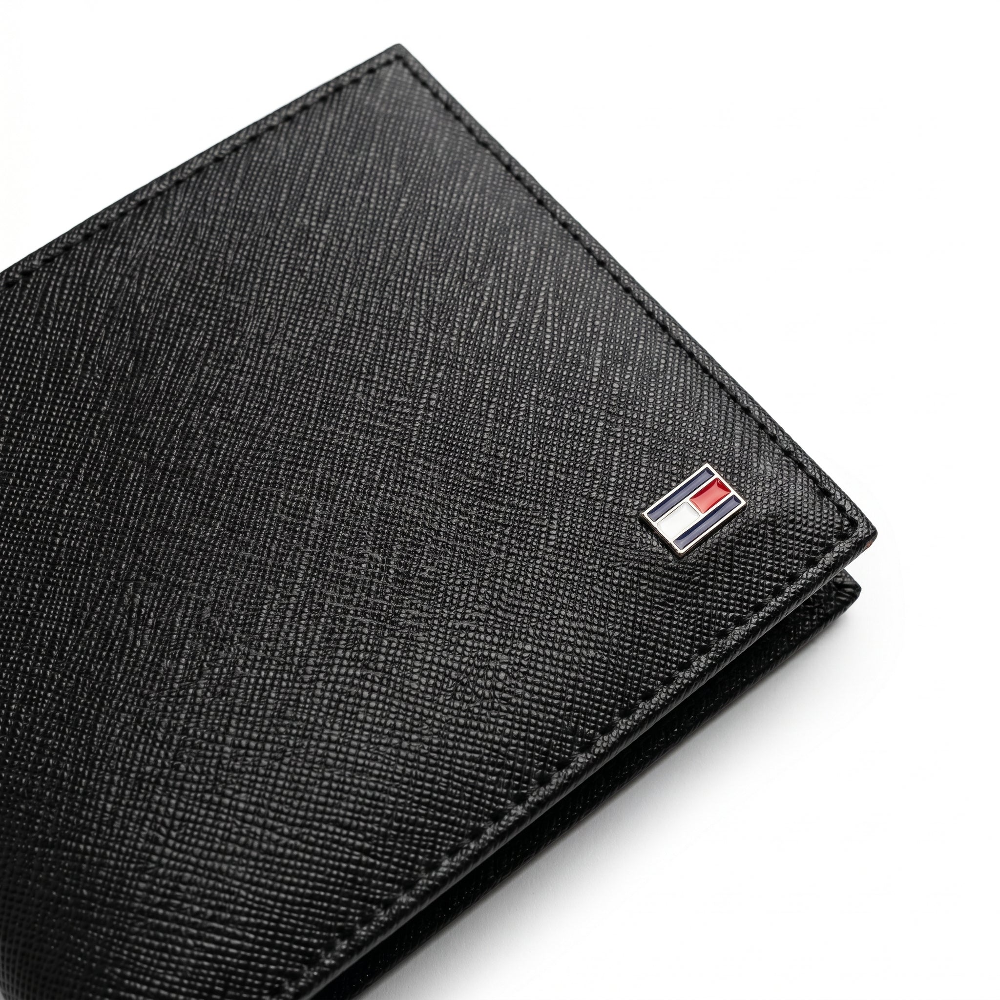 Macro close-up studio shot focusing on the iconic Tommy Hilfiger enamel flag metal logo accent over the black saffiano textured genuine leather surface