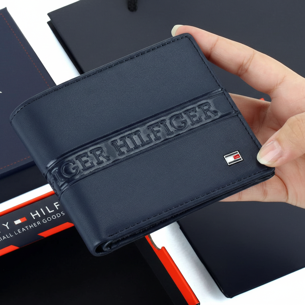 Handheld view of a Tommy Hilfiger men's navy blue leather wallet, showing its compact size and the vibrant red and white flag detail