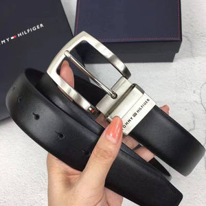 Hand holding Tommy Hilfiger black leather belt featuring classic silver prong buckle with engraved branding