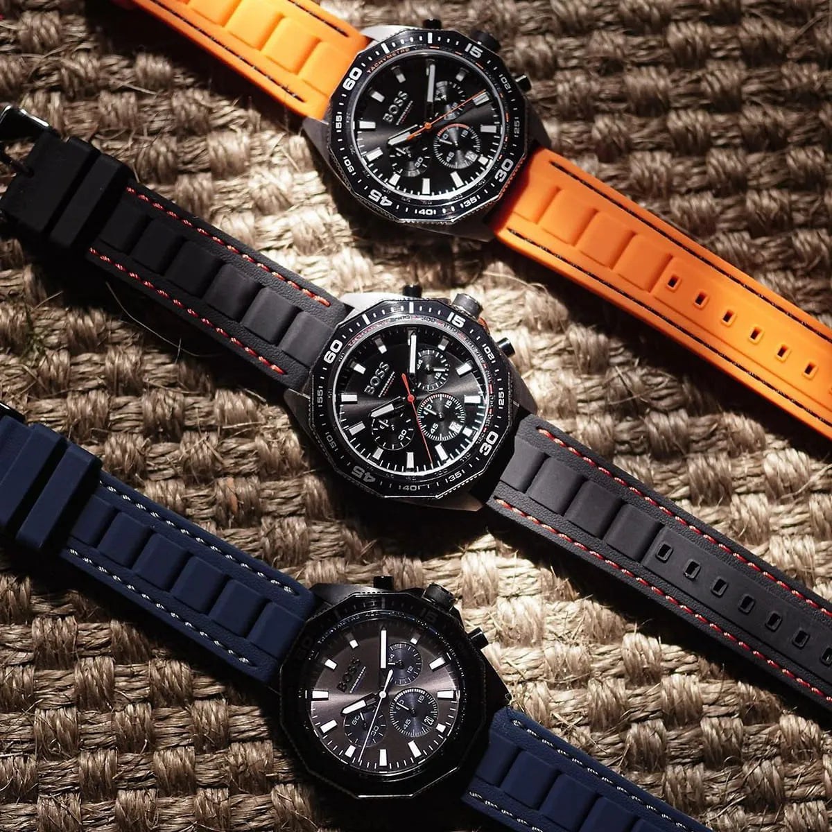 Three watches with different colored straps on a textured surface