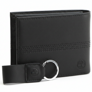 Side perspective of a standing Timberland black leather bifold wallet highlighting the vertical stitch detail and embossed tree logo next to its matching keychain