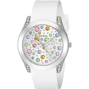 A white Guess watch with a white silicone strap, a silver-tone case accented with clear crystals, and a white dial decorated with colorful gem-like hour markers.