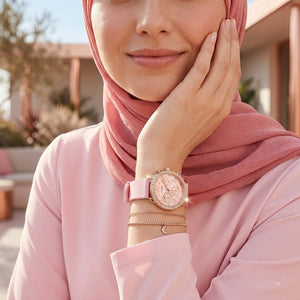 Elegant woman wearing Guess Solar W1135L2 women's quartz battery multi-function gold watch with light pink rubber strap, adding distinctive casual luxury style