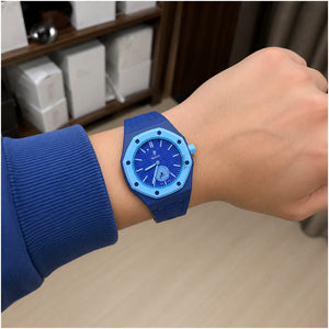 A blue watch with a matching blue strap and light blue bezel, worn on a person's wrist. The watch has a blue dial with white markings and a date window.