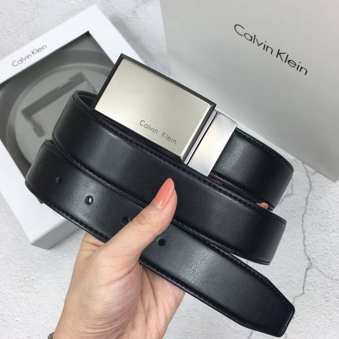 Hand holding Calvin Klein leather belt showing holes and plaque buckle