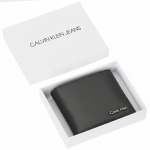Top-down view of a Calvin Klein men's black smooth leather bifold wallet featuring a silver metal logo, presented inside its original white branded gift box