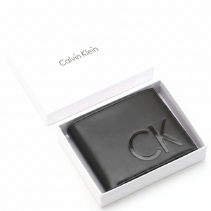 Top-down view of a Calvin Klein men's black smooth leather wallet with a large debossed CK logo, securely placed inside an open white branded gift box