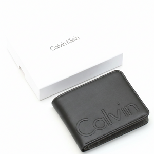 A closed Calvin Klein men's black leather wallet featuring a large debossed Calvin logo, placed next to its matching closed white branded gift box
